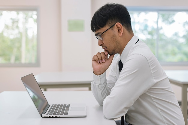 Foto giovane uomo d'affari attraente che pensa con il computer portatile del computer all'ufficio