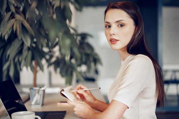 彼女の職場でメモ帳にメモを作る若い魅力的な女性実業家