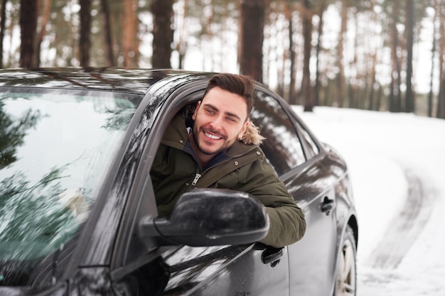 若い魅力的な白人男性は晴れた冬の日に彼の車のホイールに座っています