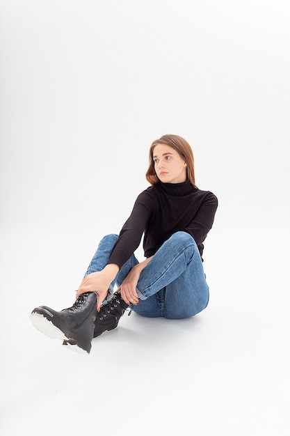 Young attractive caucasian woman in black turtleneck, blue jeans at white studio