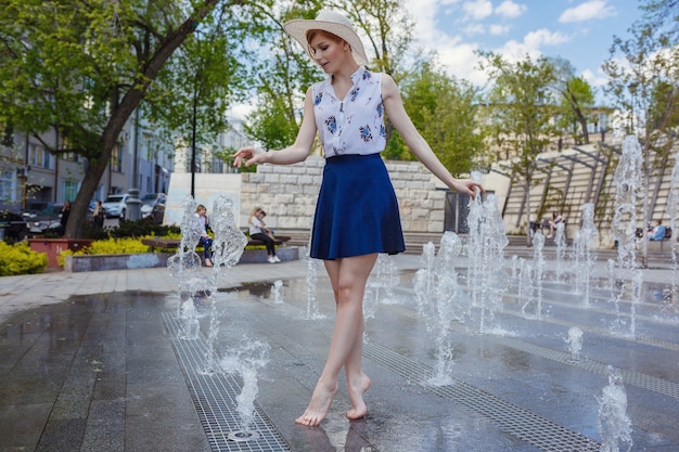 Young attractive cheerful woman walking in city. Girl enjoys playing in the fountain, refreshing coolness in summer