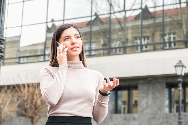 Giovane imprenditrice attraente e fiduciosa parlando al telefono davanti al business center