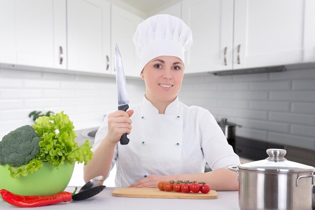 Young attractive cook woman in uniform cooking salad in modern kitchen