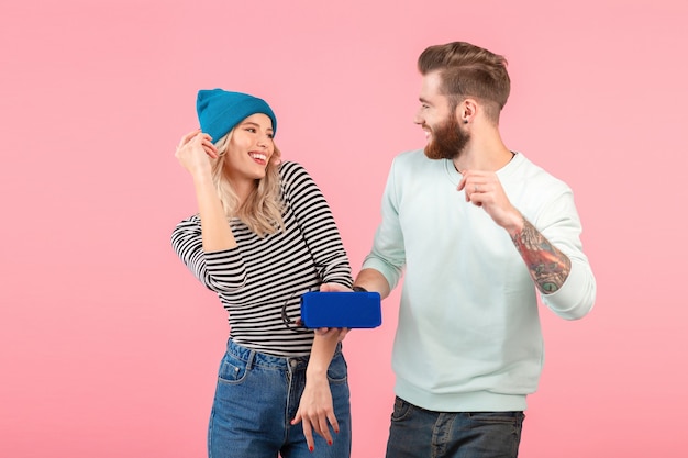 Young attractive couple listening to music on wireless speaker wearing cool stylish outfit