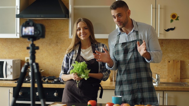 Young attractive couple shooting video food blog about cooking on dslr camera in the kitchen