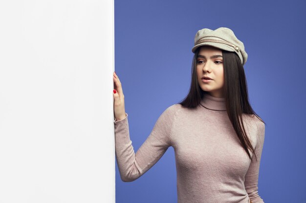 Young attractive cute Young woman standing alongside empty white billboard wall