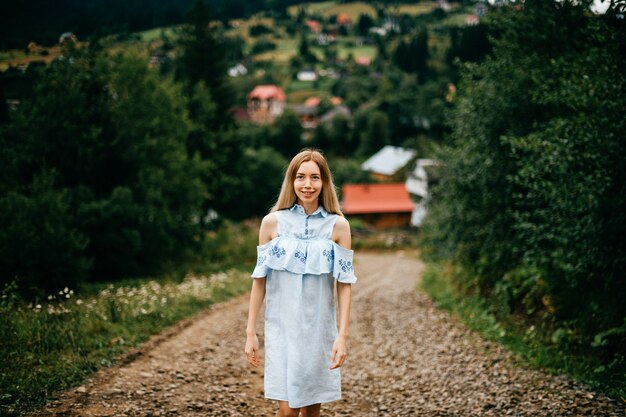 Young attractive elegant blonde girl in blue romantic dress posing on the road in the countryside