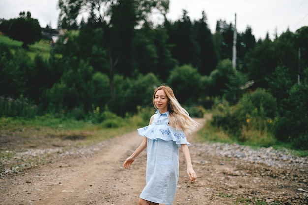 Young attractive elegant blonde girl in blue romantic dress posing on the road in the countryside