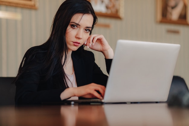 Young attractive emotional girl in business-style clothes sitting at a desk on a laptop 