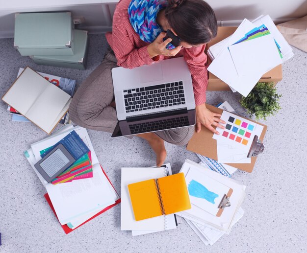 Young attractive female fashion designer working at office desk drawing while talking on mobile