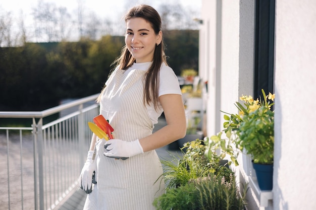 Young attractive female in overall with garden tools stand on balcony and preparing for landing