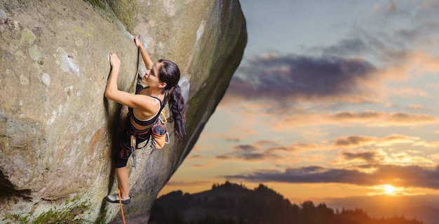 Young attractive female rock climber climbing challenging route on steep rock wall