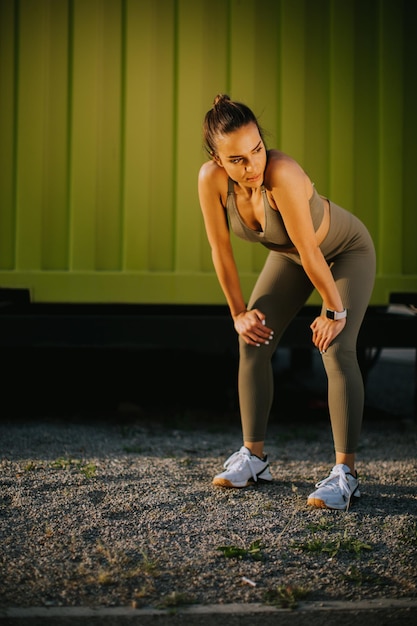 Young attractive female runner taking break after jogging outdoors