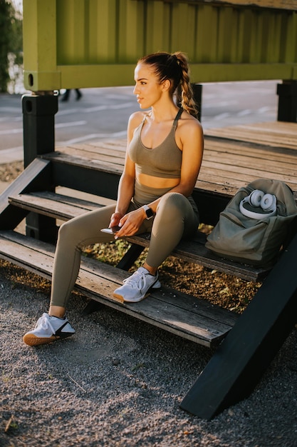 Young attractive female runner taking break after jogging outdoors