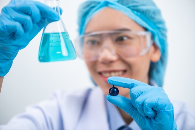 Young attractive female scientist with protective eyeglasses and mask holding a transparent pill 