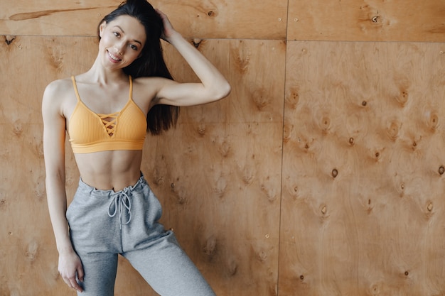 Young attractive fitness girl standing near the window on a wooden wall, resting on yoga classes