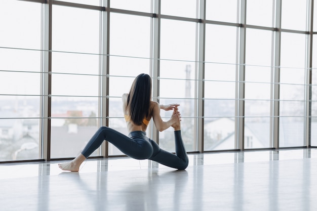 Young attractive girl doing fitness exercises with yoga on the floor. panoramic windows