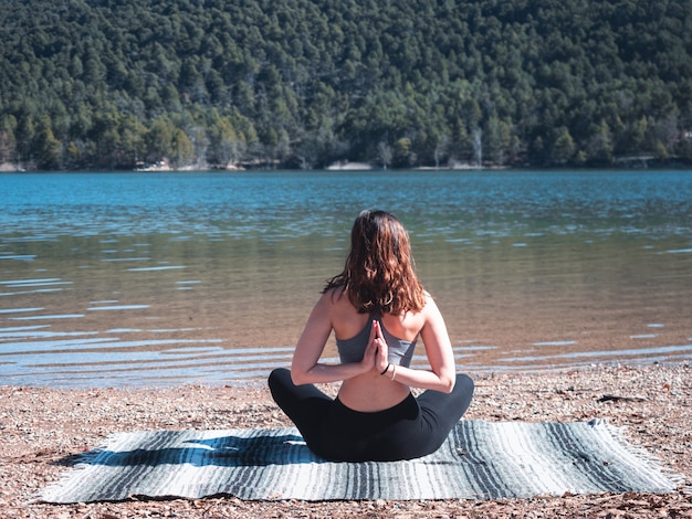 Ragazza giovane e attraente che fa yoga all'aperto, accanto a un lago, circondato dalla natura. concetto di vita sana.