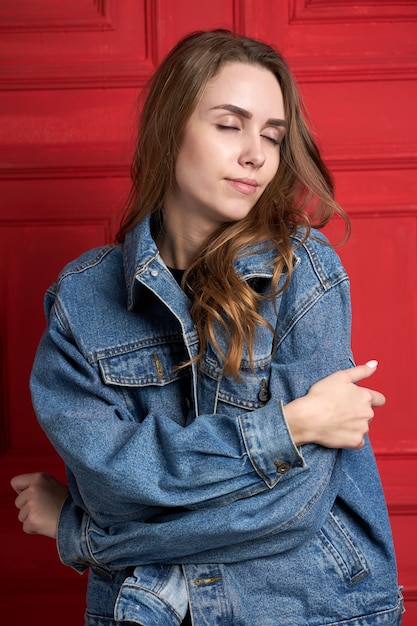 Young attractive girl or model with long hair dressed in a denim jacket and black pants siting on the chair.