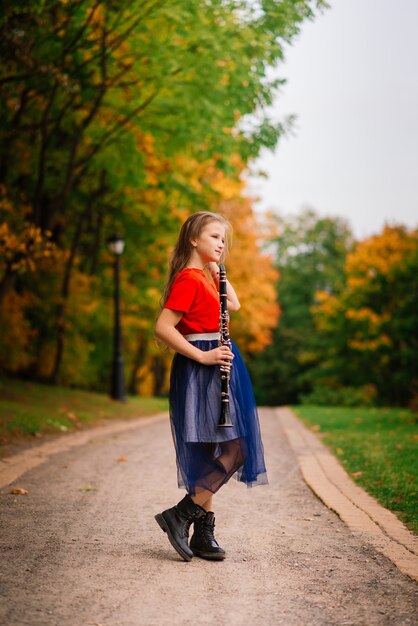 Young attractive girl playing clarinet, ebony in fall park