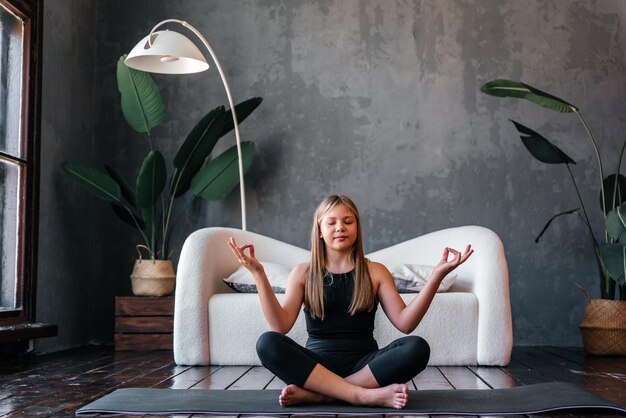 ハーフ ロータス運動アルダ Padmasana ポーズ瞑想セッション ホーム インテリアに座ってヨガを練習している若い魅力的な女の子