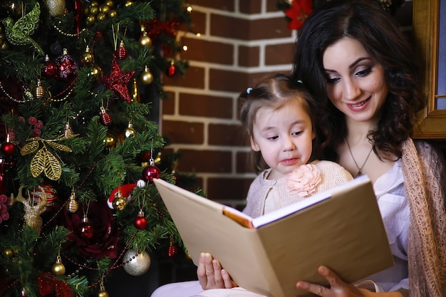 Young attractive girl wearing warm pajamas and a bedspread near the New Year tree. Christmas atmosphere.