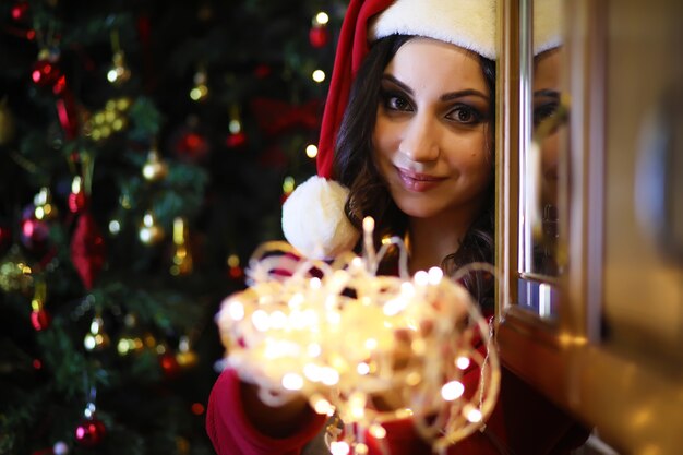 Молодая привлекательная девушка в теплой пижаме и покрывале возле новогодней елки. Рождественская атмосфера.
