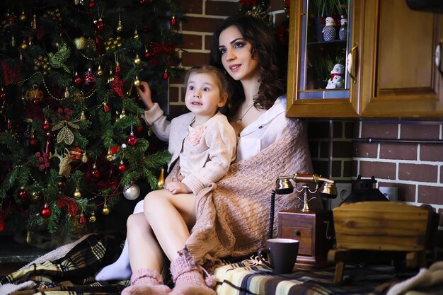 Young attractive girl wearing warm pajamas and a bedspread near the New Year tree. Christmas atmosphere.