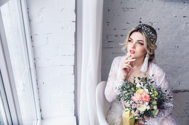 Young attractive girl with bouquet in lingerie and peignoir near window