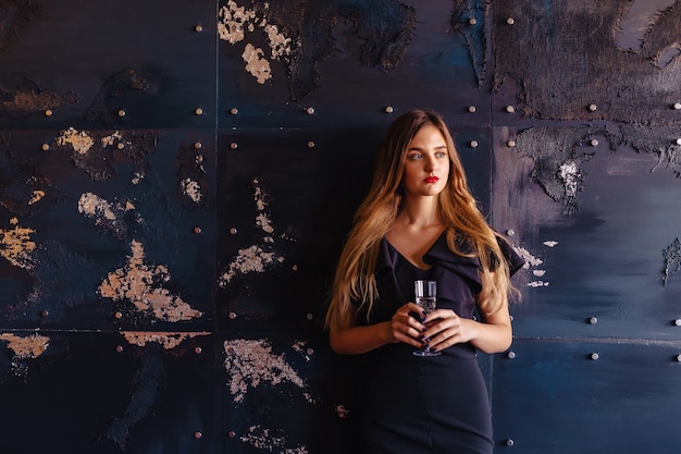 Young attractive girl with a glass of champagne or wine on the background of the wall