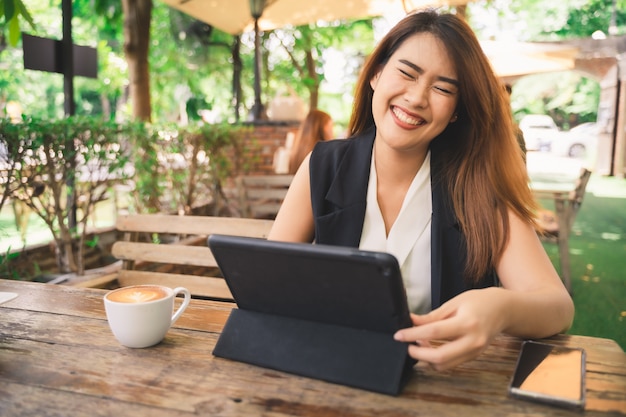 Young attractive happy Asian woman is using tablet with smile face in coffee shop cafe, online content 