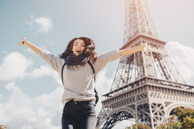 Giovane donna felice attraente che salta di gioia contro la torre eiffel a parigi, francia. ritratto di