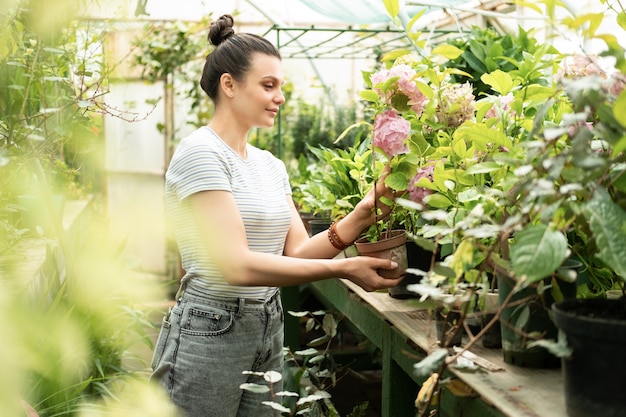 Young attractive happy women in casual clothes holding pot with Hydrangea in greenhouse.