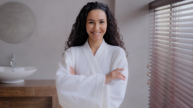 Молодая привлекательная латиноамериканка, стоящая в халате в ванной комнате, позирует со скрещенными руками