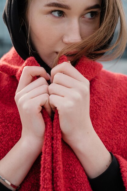 Young attractive long girl lady closeup Beautiful woman putting on a hood in a red coat Street style female portrait