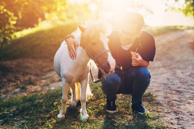 Young attractive male veterinarian examining and feeding adorable little pony horse.