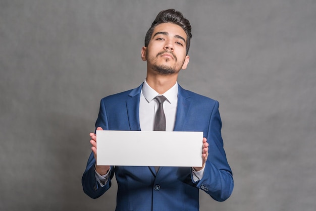 Photo young attractive man in a blue suit holding a white sign on a gray background isolated