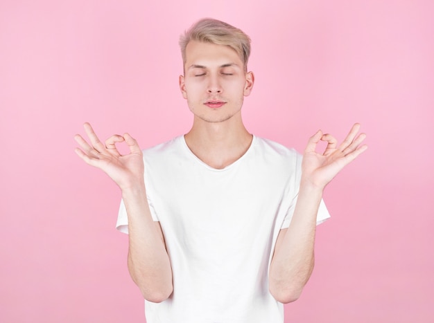 Young attractive man meditates in the lotus position over pink background.