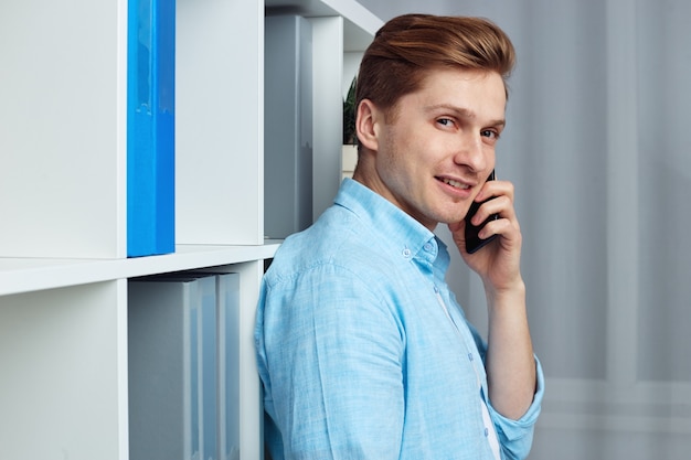 Young attractive man speaking on smartphone while standing in office