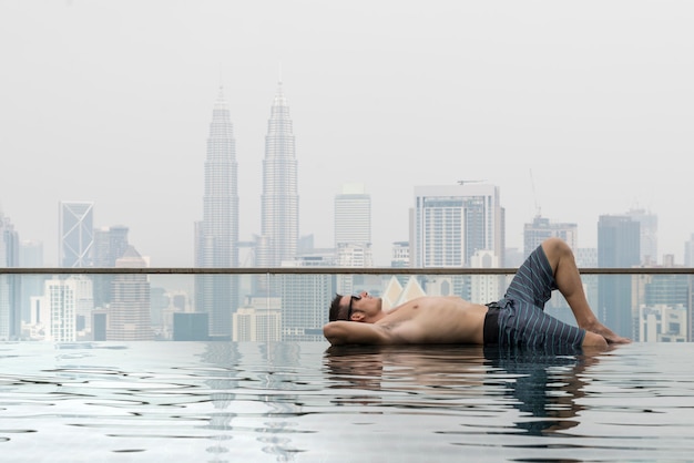 young attractive man with sunglasses on the swimming pool in roof at skyscraper. Is in Kuala Lumpur