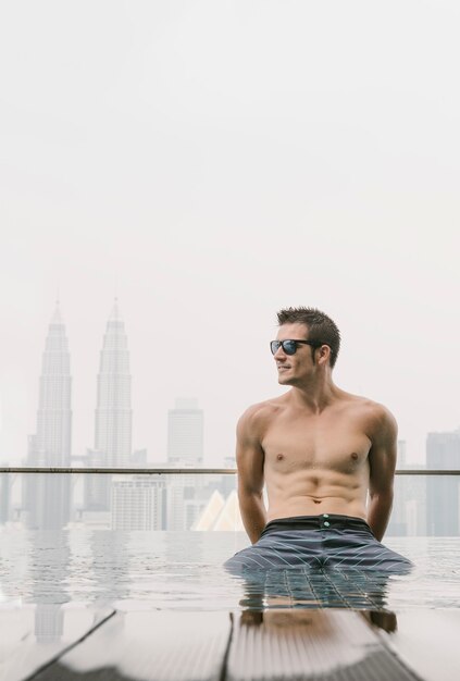 young attractive man with sunglasses on the swimming pool in roof at skyscraper. Is in Kuala Lumpur