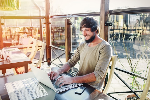 Giovane uomo attraente che lavora con il computer portatile nel caffè all'aperto