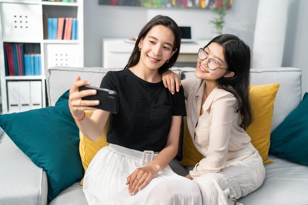 Young attractive mom and her beautiful teenage daughter with glasses are sitting on the couch