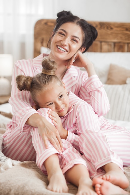 Young attractive mother and her little daughter having fun at pajamas party. Family in the morning