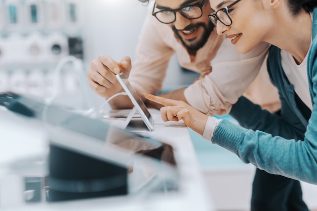 Young attractive multicultural couple with eyeglasses trying out tablet in tech store.