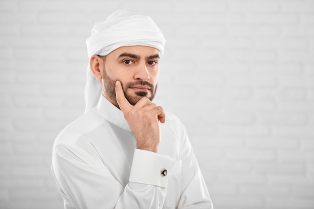 Giovane maschio musulmano attraente nel tradizionale cloting islamico pensando a qualcosa