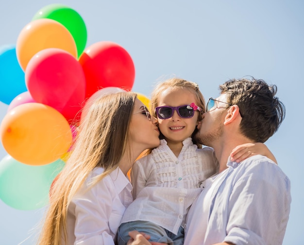 Young attractive parents with balloons kissing their little daughter on the cheek.