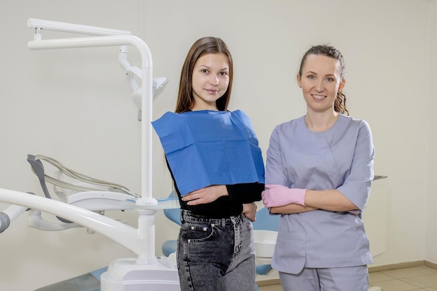 Young attractive patient and young female dentist standing and\
smiling in the background the workplace of the dentist with\
tools