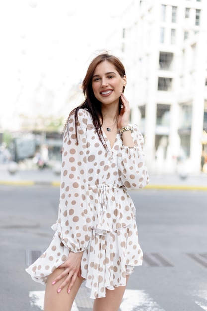 Young attractive pensive woman beautiful dress thoughtfully looking in camera standing on cozy city street