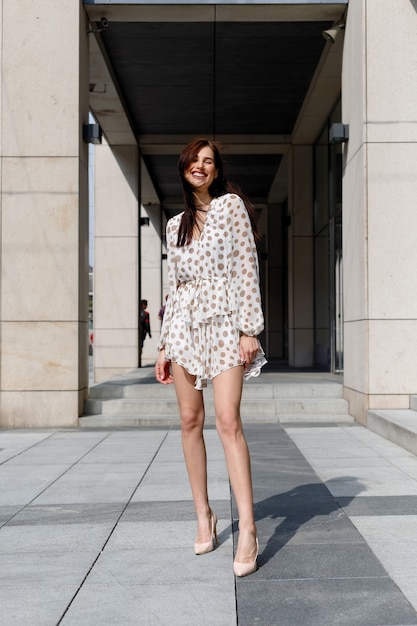 Young attractive pensive woman beautiful dress thoughtfully looking in camera standing on cozy city street